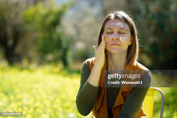 young woman applying sunscreen in the countryside - woman face hat foto e immagini stock