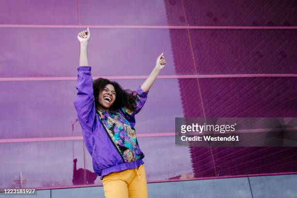 young woman with urban look cheering in front of pink glass wall - cheering stock-fotos und bilder