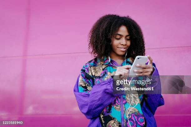 young woman typing on smartphone and listening to music - viola colore foto e immagini stock