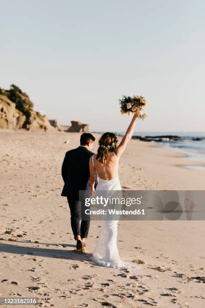 rear view of happy bridal couple walking at the beach - beach wedding stock pictures, royalty-free photos & images