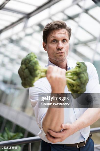 businessman doing weight training with broccoli - funny vegetable stockfoto's en -beelden