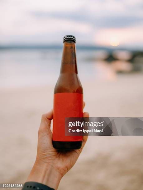 beer bottle with blank label on beach at sunset - garrafa de cerveja imagens e fotografias de stock