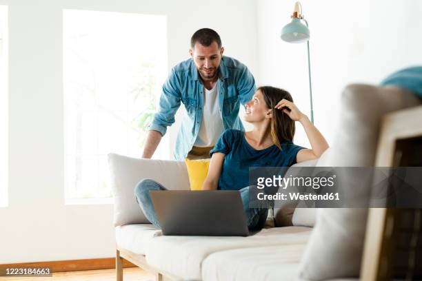 young couple on couch at home with laptop - paar beratung stock-fotos und bilder