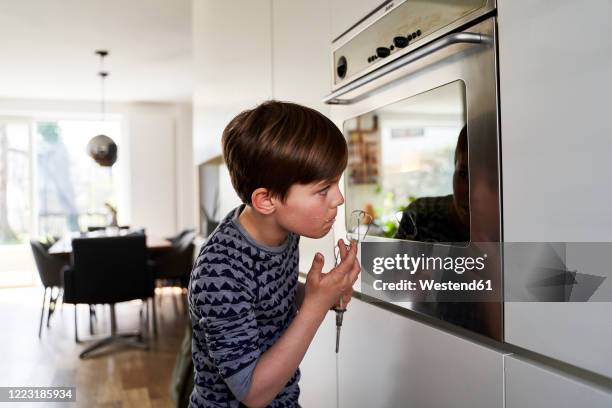 boy tasting batter while watching his mirror image on surface of oven - looking back stock-fotos und bilder