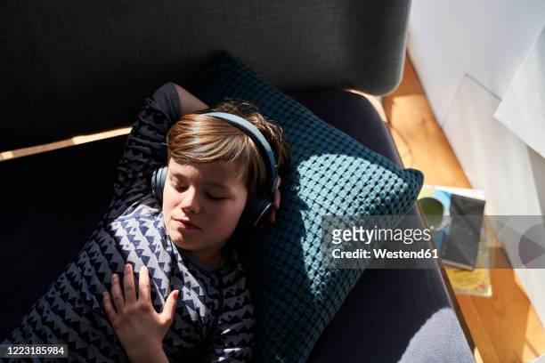 portrait of boy lying on couch listening music with headphones - boy headphones stock-fotos und bilder