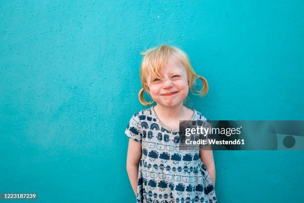 portrait of grinning little girl in front of blue wall - blonde girl smiling stock-fotos und bilder