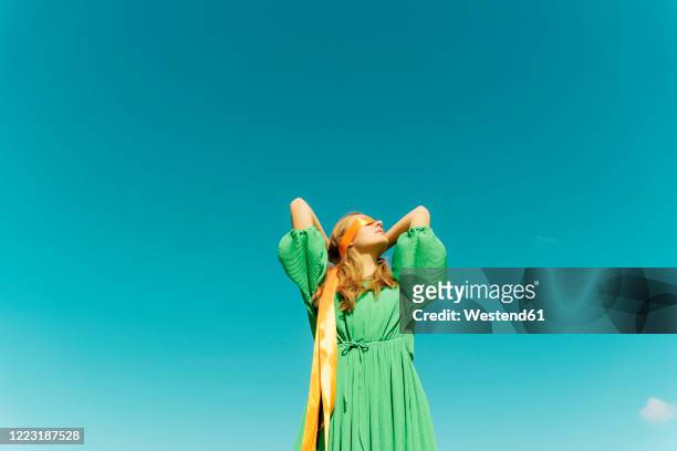 blindfolded young woman wearing a green dress under blue sky - hände hinter dem kopf stock-fotos und bilder