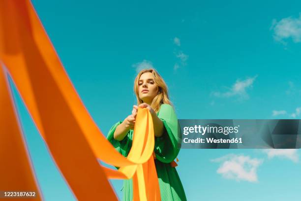 portrait of young woman wearing a green dress holding orange ribbons - green dress stock pictures, royalty-free photos & images