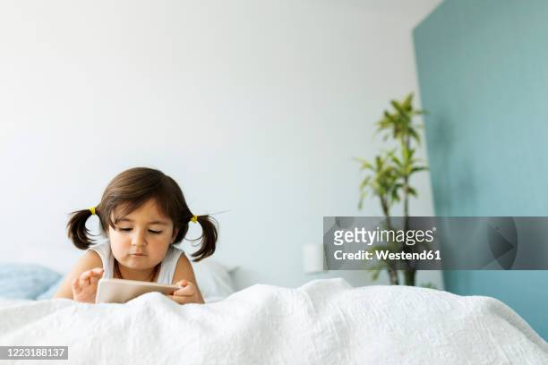 portrait of little girl lying on bed using at smartphone - 3 years brunette female alone caucasian stock pictures, royalty-free photos & images