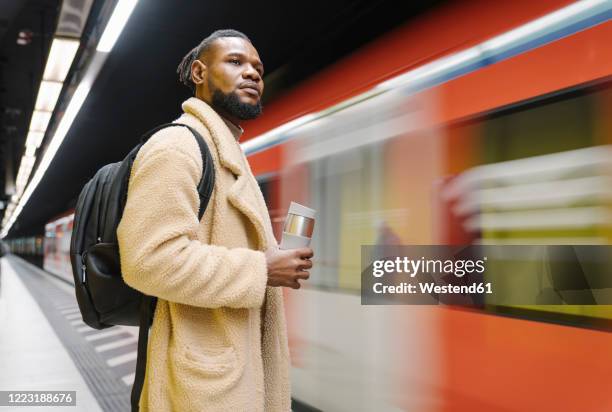 stylish man with reusable cup and headphones in a metro station - business person driving stock-fotos und bilder