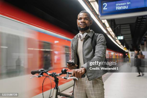 stylish man with a bicycle, headphones and smartphone in a metro station - pendler bahn stock-fotos und bilder