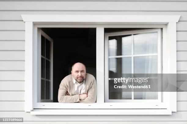 portrait of mature man leaning out of window of his house - fenster stock-fotos und bilder