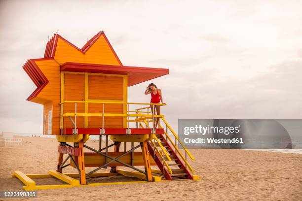 woman in red swimsuit on lifeguard hut on miami beach, miami, florida, usa - strandwächterhaus stock-fotos und bilder