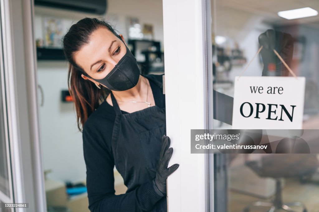 Happy business owner hanging an open sign during COVID-19