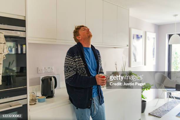 man struggling with flu like symptoms in the kitchen - atemlos stock-fotos und bilder