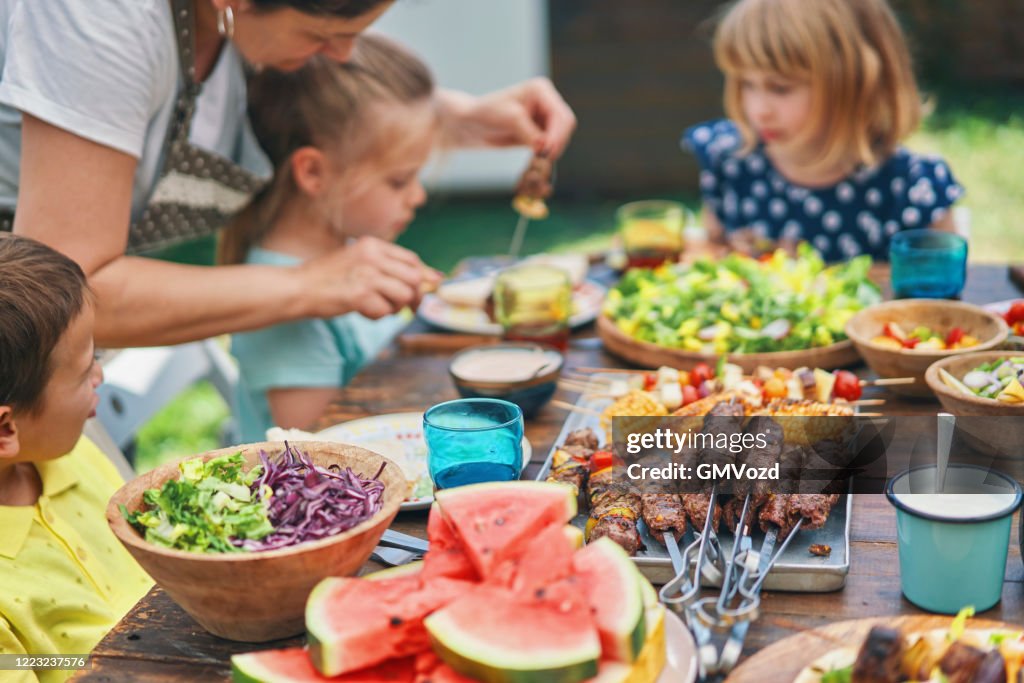 Young Family Eating Lamb, Beef and Vegetable Kebab with Green Salad Outside