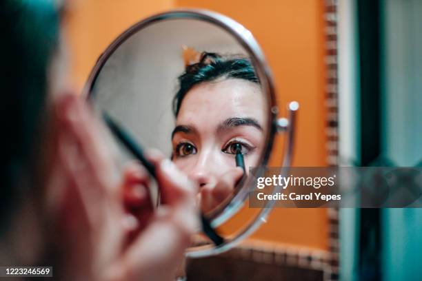 young teenager applying eyeliner in domestic bathroom - lápiz de ojos fotografías e imágenes de stock