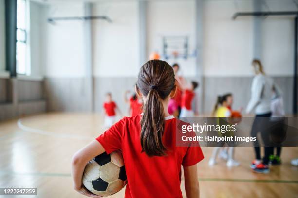 rear view of small girl standing with ball indoors in gym class, physical education concept. - calcio sport foto e immagini stock