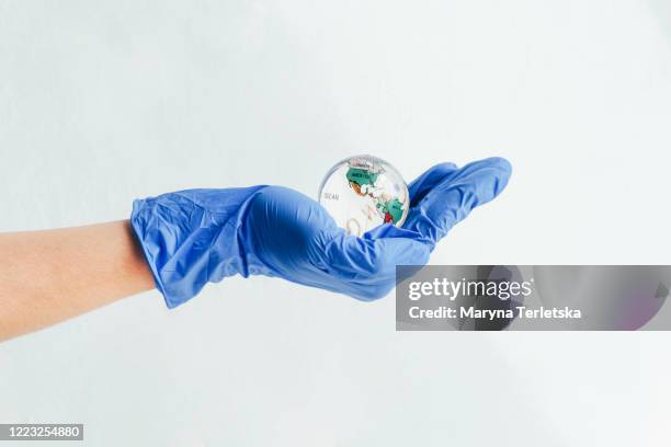 a hand in a medical glove holds a glass globe. - handschuh karte stock-fotos und bilder
