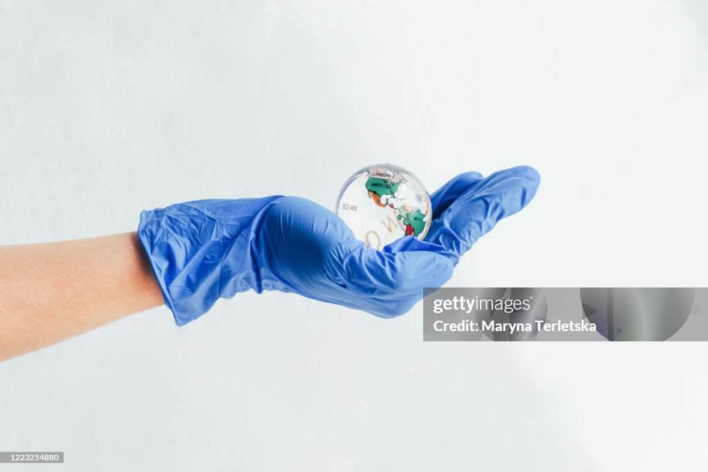 A hand in a medical glove holds a glass globe.