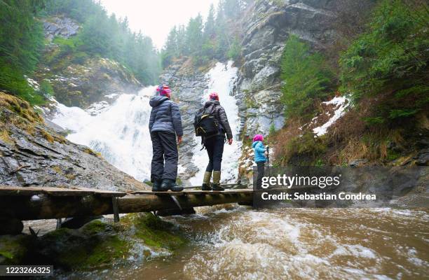 three females tourists amazed by the beauty of the ice waterfall in winter. - family hiking in spring outdoors foto e immagini stock