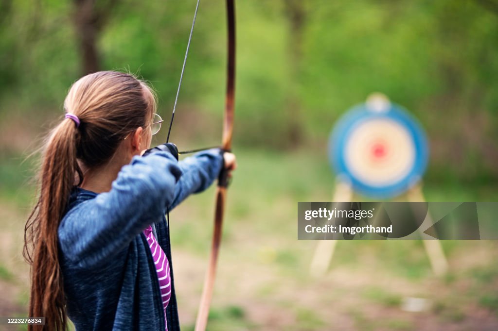 Adolescente tirant l’arc à la cible dans la forêt