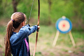 Teenage girl shooting bow at target in the forest