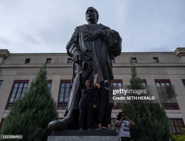 Protesters raise their fists as they stand on the base of a statue of Christopher Columbus in front of City Hall during an "International March for...