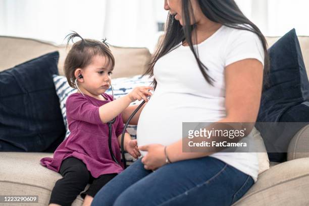 toddler uses stethoscope on mom's pregnant belly. - prenatal care stock pictures, royalty-free photos & images