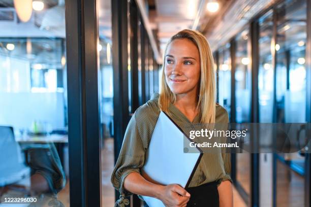 young businesswoman standing in office hallway with laptop - standing with laptop imagens e fotografias de stock