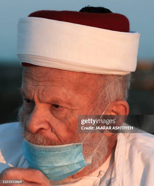 An elderly Samaritan, wearing a face mask due to the novel coronavirus, joins others to pray on top of Mount Gerizim near the northern West Bank city...