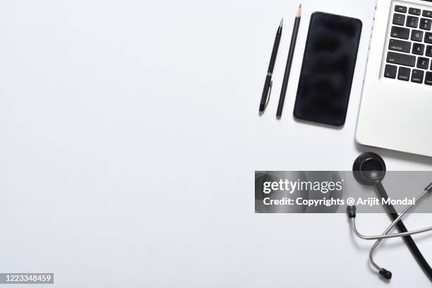 medical doctor's work place with smartphone, personal computer, stethoscope, pens white background top view - aerial view desk stock pictures, royalty-free photos & images