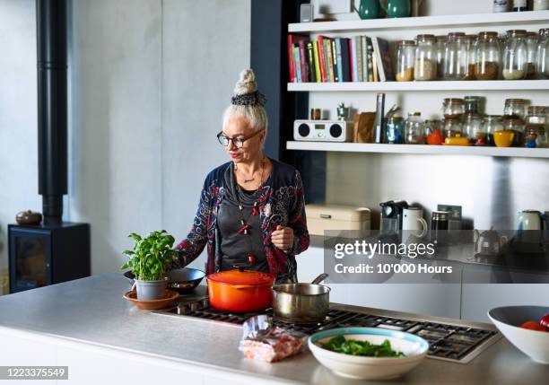 senior woman making meal at home with fresh ingredients - hob fotografías e imágenes de stock