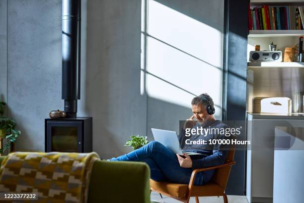mature man listening to music on laptop - at home stock-fotos und bilder