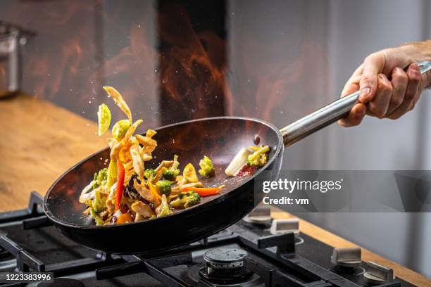 chef wirft flammendes gemüse - pots and pans stock-fotos und bilder