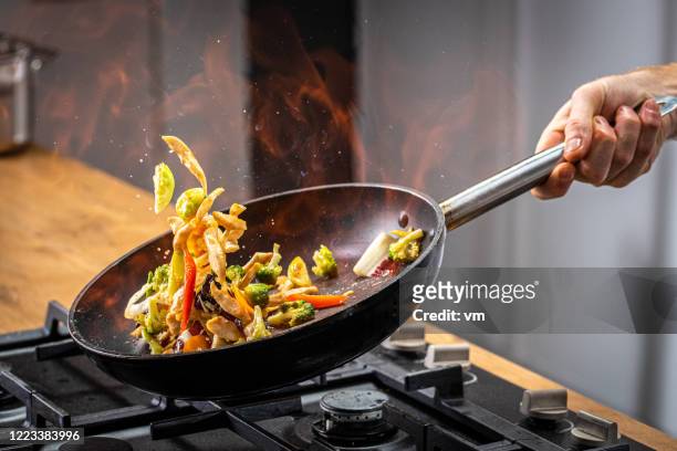chef-kok die vlammende groente wegdraagt - braadpan stockfoto's en -beelden