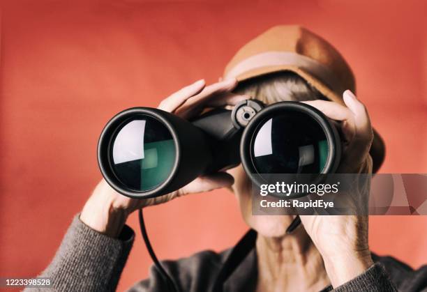 senior woman peers curiously through binoculars, - see the bigger picture stock pictures, royalty-free photos & images