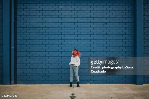 happy young girl shaking her hair in front of blue brick wall - brick wall stock pictures, royalty-free photos & images