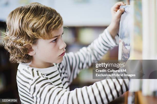 boy selecting book from shelf in library - differential focus education reach stockfoto's en -beelden