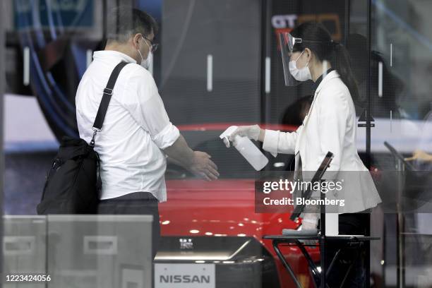 Showroom assistant wearing a protective mask and face shield, right, sprays hand sanitizer into a visitor's hands at the entrance of Nissan Motor...