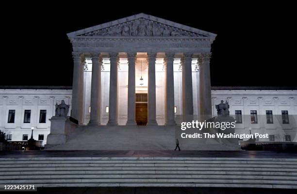 The Supreme Court building glows in the night as a lone Supreme Court Police Officer walks the steps in the overnight hours of March 18, 2020. The...
