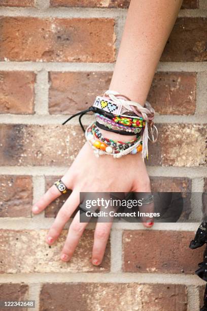 woman's hand with bracelets by brick wall - friendship-bracelet fotografías e imágenes de stock