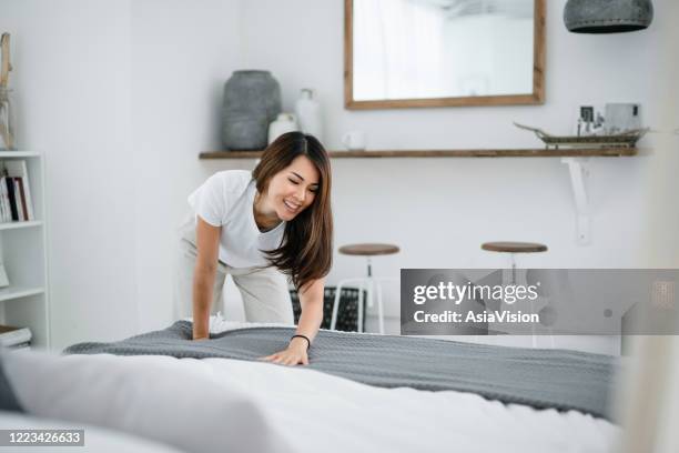 young asian woman doing her morning routine, arranging pillows and making up bed at home - tidy bedroom stock pictures, royalty-free photos & images