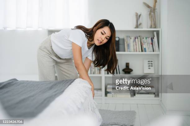 young asian woman doing her morning routine, arranging pillows and making up bed at home - tidy bedroom stock pictures, royalty-free photos & images