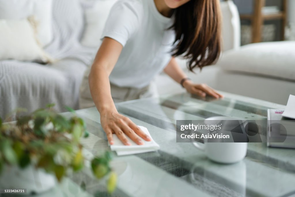 Recortado tiro de joven mujer asiática ordenando la sala de estar y limpiando la superficie de la mesa de café con un paño