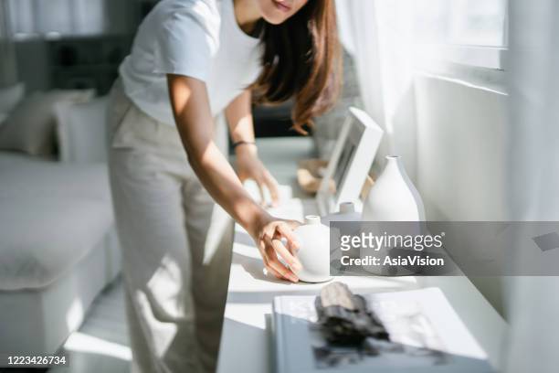 la giovane donna asiatica si gode il suo tempo a casa, decorando e organizzando cornici e vasi sullo scaffale vicino alla finestra - arrangiare foto e immagini stock