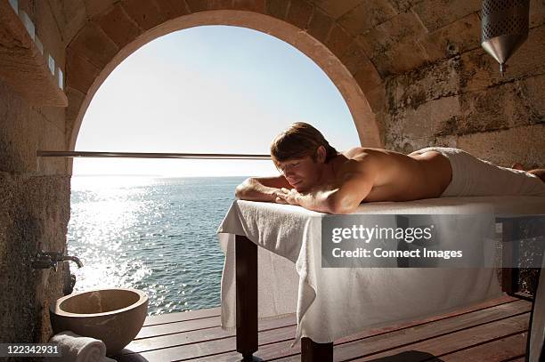 man lying on massage table by the ocean - spa treatment stock pictures, royalty-free photos & images