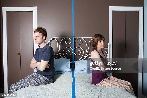 young couple sitting on bed separated by blue line - teimoso - fotografias e filmes do acervo