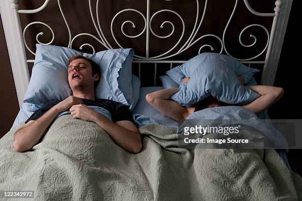 young man snoring, woman covering face with pillow - couple sleeping fotografías e imágenes de stock