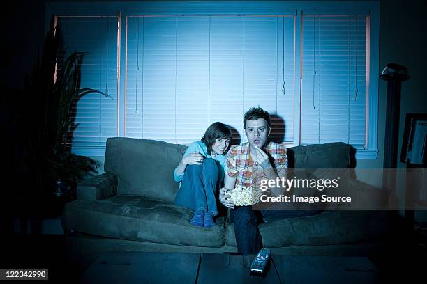 young couple watching tv, man eating popcorn - horror movie stock-fotos und bilder